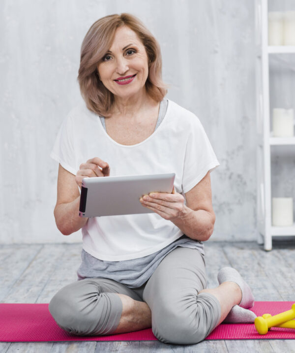 happy-senior-woman-using-laptop-near-yoga-equipment